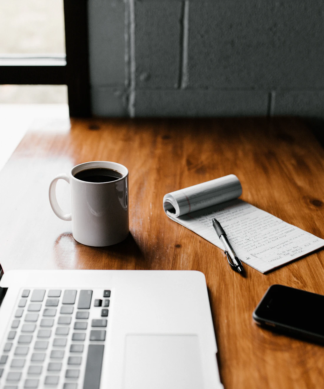 A laptop, coffee and handwritten notes on a wooden desk